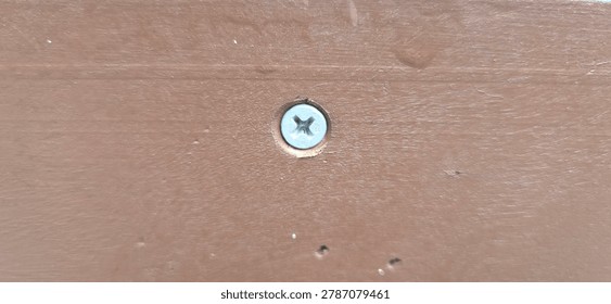Close-up of a Phillips screw fixed into a brown wooden surface. Detailed view of wood panel and metal screw suitable for carpentry, DIY projects, furniture construction, and building material concepts.