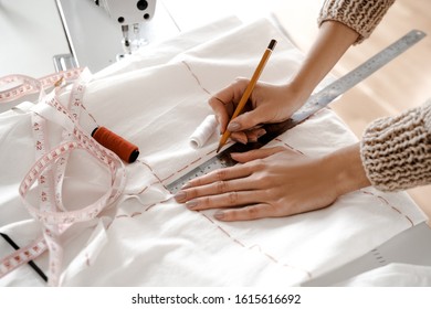 Closeup Photo From Above, Hands On The Seamstress Table, Creative Space, Hands Draw Markup For A New Garment On A White Cloth, Make Notes With A Ruler And Thread Near The Sewing Machine