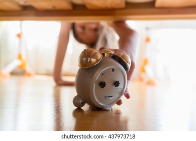 Closeup Photo Of Beautiful Girl Reaching For Alarm Clock Under The Bed