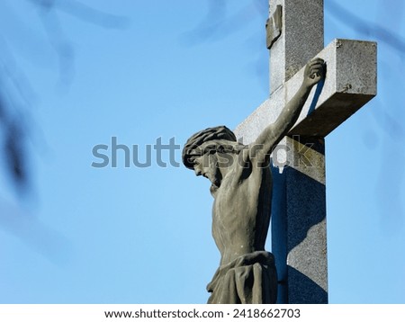 Close-up photo of a beautiful stone sculpture of Jesus on the cross with a clear blue sky in the background placed in the city cemetery of Zapresic, Croatia