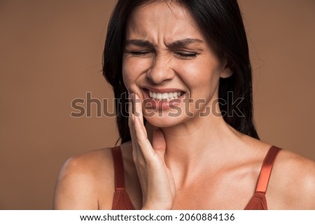 Closeup photo of brunette woman pressing her cheek with painful expression because she having terrible tooth ache, isolated on beige color background