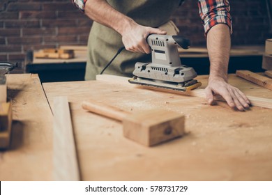 closeup photo of cabinetmaker grinds wooden plank on tabletop at workstation.