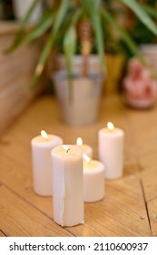 Close-up Photo Of Candles On Wooden Floor At Home, Plant In Pot In The Background. Room With Candles For Yoga Training, Calm And Beautiful View. No People. Copy Space