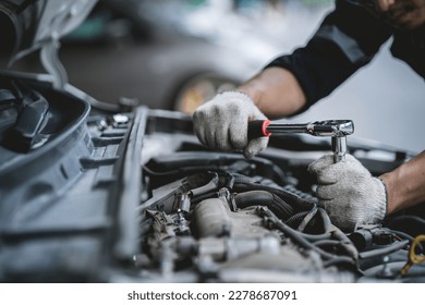 Close-up photo of a car mechanic working on a car engine in a mechanics repair service garage. A uniformed mechanic is working on a car service. Work in the garage, repair and maintenance services.