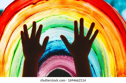 Close-up photo of child's hands touch painting rainbow on window. Family life background. Image of kids leisure at home, childcare, safety joy symbol.