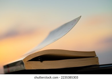 Closeup Photo of a Closed Book with a Pen Inside it over Beautiful Sunset Sky Background. Finished Reading the Book for Today. Intellectual Pastime. - Shutterstock ID 2235385303