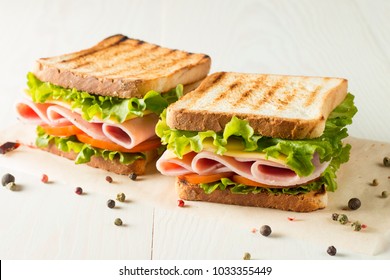 Close-up photo of a club sandwich. Sandwich with meet, prosciutto, salami, salad, vegetables, lettuce, tomato, onion and mustard on a fresh sliced rye bread on wooden background. Olives background.