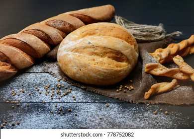 Close-up photo of composition of fresh handmade white bread on dark wooden table with flour around.