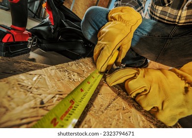 Closeup Photo of Construction Worker in Yellow Protective Gloves Measuring the Oriented Strand Board with Tapeline Before Making a Cut. - Shutterstock ID 2323794671