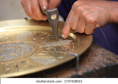 Closeup photo of craftsman's hands holding small hammer and working with traditional bronze plate decorated by silver ornament at the market of Medina old town in Tunis, Tunisia