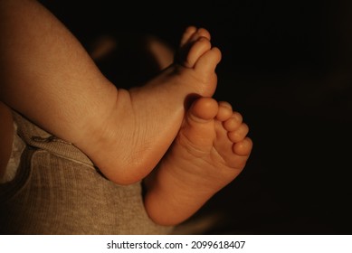 A Close-up Photo Of The Crossed Legs Of A Newborn Baby In A Bodysuit Who Is Lying On A Sofa In The Sunlight In The Evening.