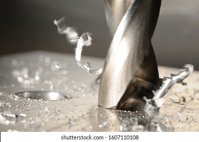 Close-up photo of drilling process with tools and metal shavings. Blurred gray background