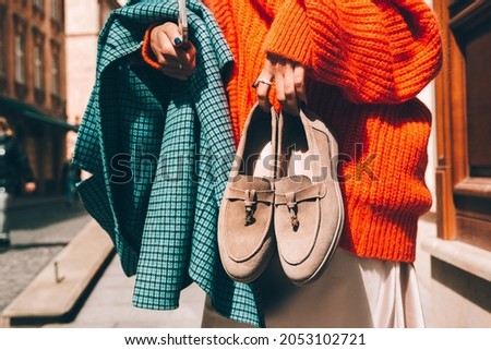 Close-up photo of fashionable women in orange sweater and beige dress holding in hands checkered coat and beige suede shoes
