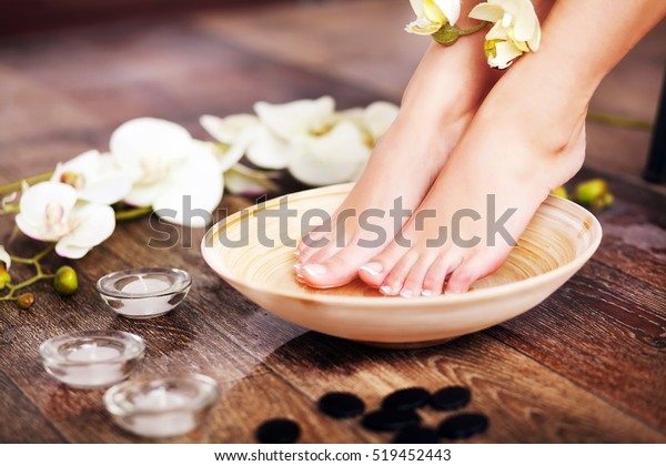 Closeup photo of a female feet at spa salon on pedicure procedure. Female legs in water decoration the flowers.