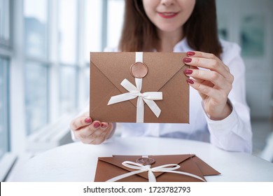 Close-up Photo Of A Female Hands Holding A Bronze Invitation Envelope With A Wax Seal, A Gift Certificate, A Card, A Wedding Invitation Card