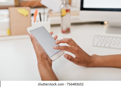 Close-up Photo Of Female Hands Holding White Phone Under Table. Girl With Brown Skin Using Smartphone And Touching Screen Sitting In Office.