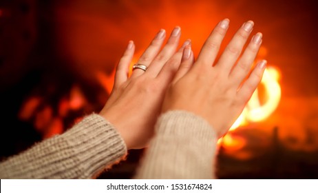 Closeup photo of female hands warming by the fireplace. Feeling cosy by the fire at home