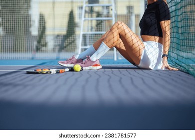 Close-up photo of female tennis player's legs sitting on tennis court near racket and ball. Tennis concept. - Powered by Shutterstock