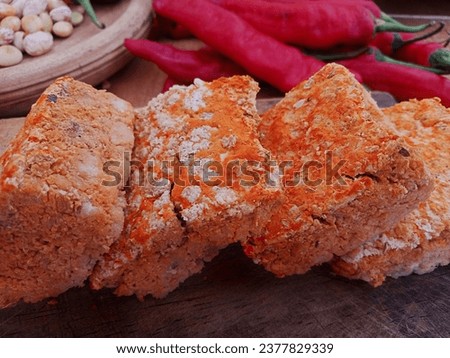 close-up photo of four pieces of orange colored oncom (tofu dregs) placed on a wooden cutting board among other kitchen spices