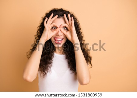 Closeup photo of funny lady playful mood holding round fingers in specs shape near eyes sticking tongue wear white casual outfit isolated beige pastel color background