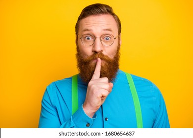 Closeup Photo Of Funny Red Head Guy Tricky Mood Hold Finger On Lips Asking Not Talk Say Speak Tell Wear Specs Bright Blue Shirt Green Suspenders Isolated Yellow Color Background