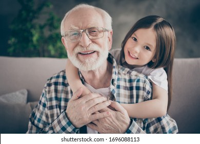 Closeup photo of funny two people old grandpa little granddaughter sitting sofa stay home quarantine safety hugging piggyback modern design interior living room indoors