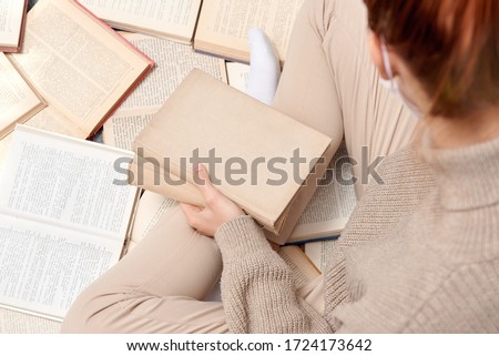 Closeup photo of a girl with a book in her hands sitting around many books. Distance learning.