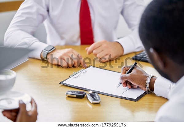 close-up photo of hands and documents of car,\
professional salesman of dealership shows on document and talks\
about all terms of sale to\
customers