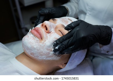 A Close-up Photo Of The Hands Of The Female Cosmetologist Rolls Up Peeling Gommage From The Woman's Face. A Doctor In Disposable Medical Gloves During A Procedure For Skin Cleaning In A Beauty Salon.