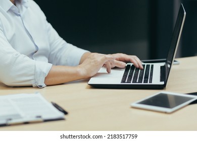 Close-up Photo. The Hands Of A Young Businessman, A Freelancer, An IT Worker In A White Shirt Who Works Behind A Laptop, Typing On A Keyboard, At A Desk In A Modern Office.