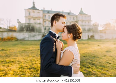 Close-up photo of happy groom kissing bride's forehead on background old castle