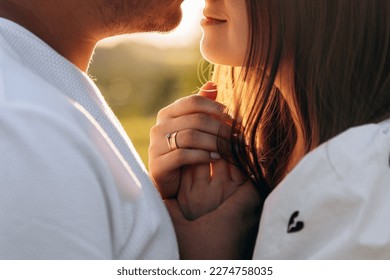 Close-up photo of a husband and wife couple kissing and holding hands in front of them. Female hand with a wedding ring. Couple man and woman at sunset. Gold wedding rings as a sign of strong love - Powered by Shutterstock