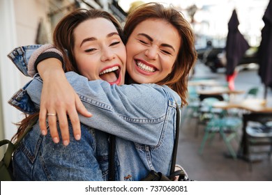 Close-up photo of laughing woman friends hugging each other on city street