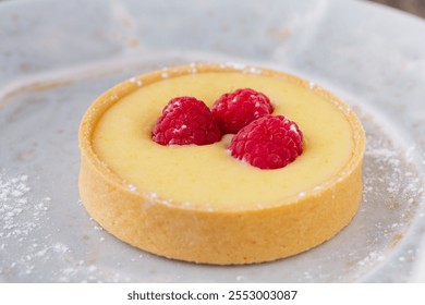 A close-up photo of a lemon tart topped with fresh raspberries, elegantly presented on a plate dusted with powdered sugar. - Powered by Shutterstock