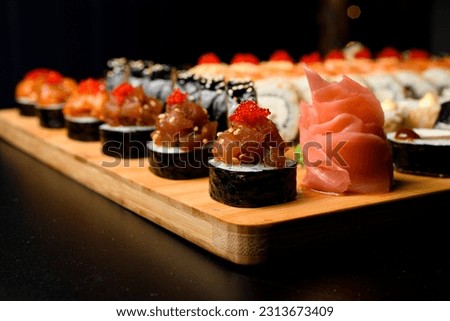 Closeup photo of maki rolls with salmon and tobiko calve on wooden serving board on dark upside. Set of rolls on blurred background.