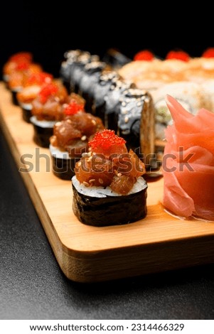 Closeup photo of maki rolls with salmon and tobiko calve on wooden serving board on dark table. Set of rolls on blurred background.