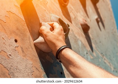 Close-up Photo Of Male Hand Gripping Climbing Holds On Worn Wall Outside. Man Doing Bouldering Exercise On Artificial Rock Climbing Wall At Park.