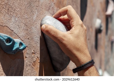 Close-up Photo Of Male Hand Gripping Climbing Holds On Worn Wall Outside.  Man Doing Bouldering Exercise On Artificial Rock Climbing Wall At Park.
