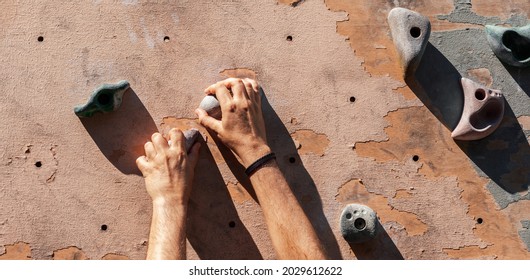 Close-up Photo Of Male Hands Gripping Climbing Holds On Worn Wall Outside.  Man Doing Bouldering Exercise On Artificial Rock Climbing Parkour At Park.