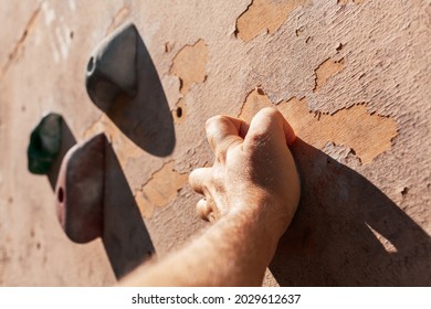 Close-up Photo Of Male Hands Gripping Climbing Holds On Worn Wall Outside.  Man Doing Bouldering Exercise On Artificial Rock Climbing Wall At Park.