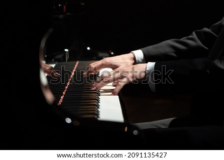 Close-up photo of male person hands in a black jacket and white shirt playing black and white piano keys. Musical instrument and music.