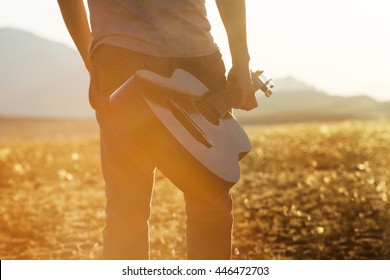 Closeup photo of man with guitar on sunset backdrop 