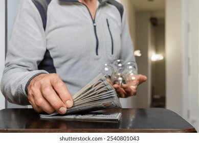 Closeup photo of man with light bulbs counting money. Brighten your budget: an incandescent lamp with scattered dollar bills, reminding homeowners of their electricity expenses and savings - Powered by Shutterstock