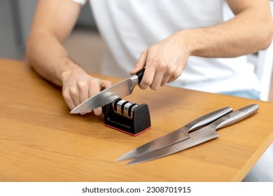 Close-up photo of man sharpening knives with special knife sharpener at home