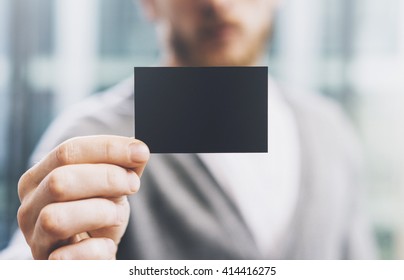 Closeup photo man wearing casual shirt and showing blank black business card. Blurred background. Ready for private information. Horizontal mockup