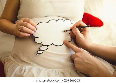 Closeup of photo of man writing on paper sign on wife's pregnant abdomen