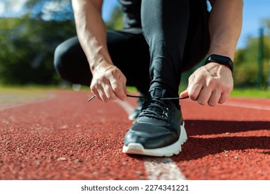 Close-up photo of a man's hand tying shoelaces at a sports stadium, a runner before starting a run and training, on a sunny day.
