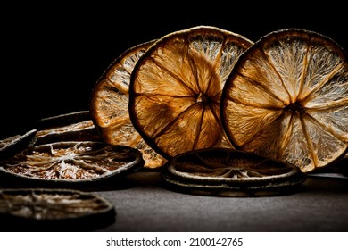 Closeup photo of many dried lemon slices lit from behind over a dark surface and black background. 