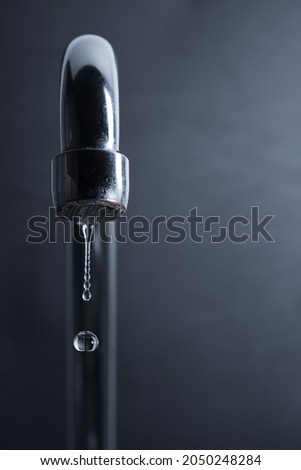 Closeup photo of a metallic faucet with water drops on a black background. Leaking faucet.