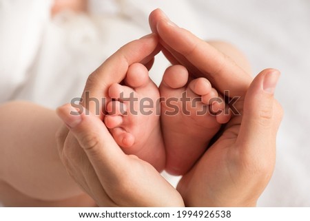 Closeup photo of newborn's feet in mother's palms on isolated white textile background